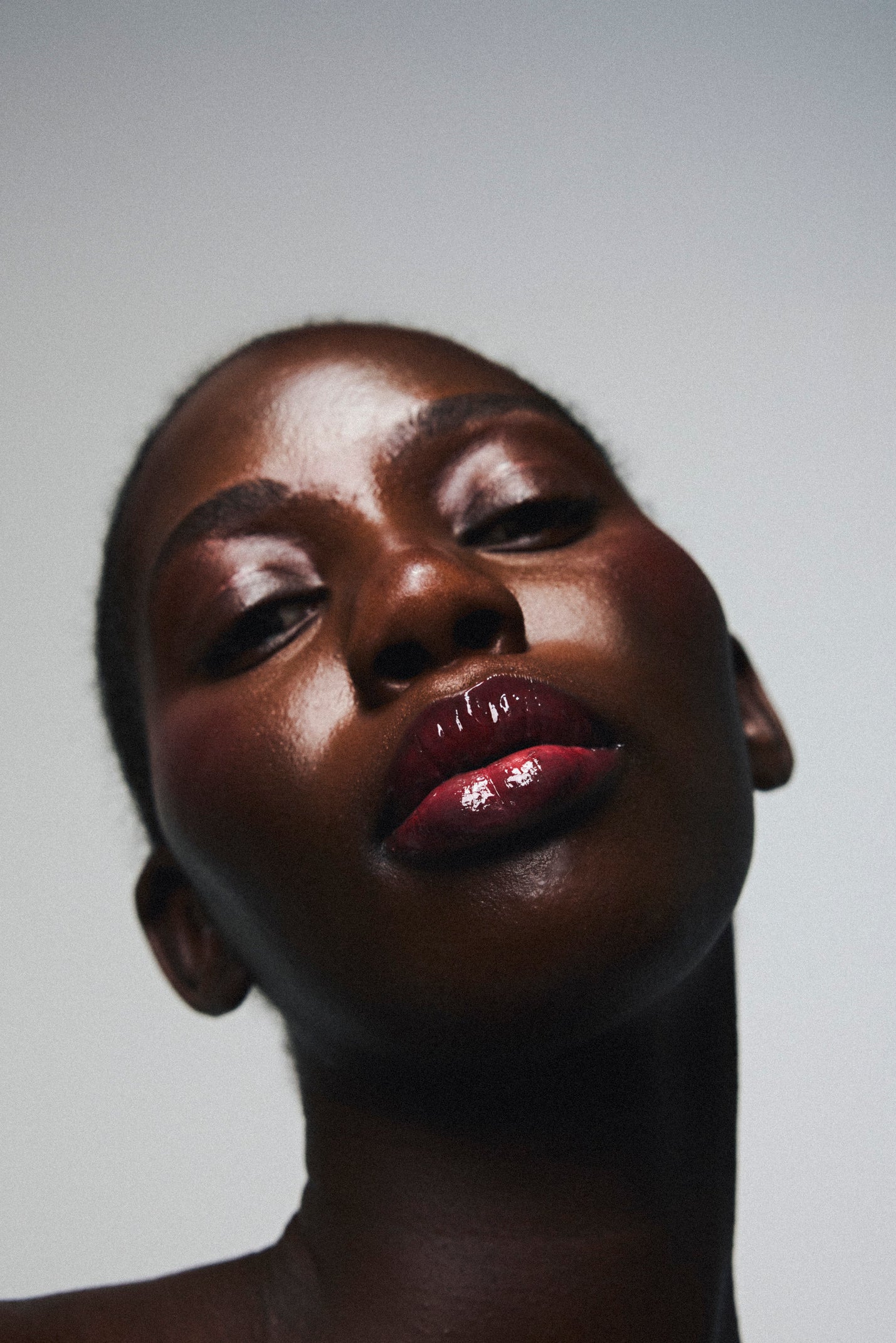 Application du gloss à lèvres éclat nourrissant Melayci, teinte Cherry rouge, sur une femme à la peau noire.
